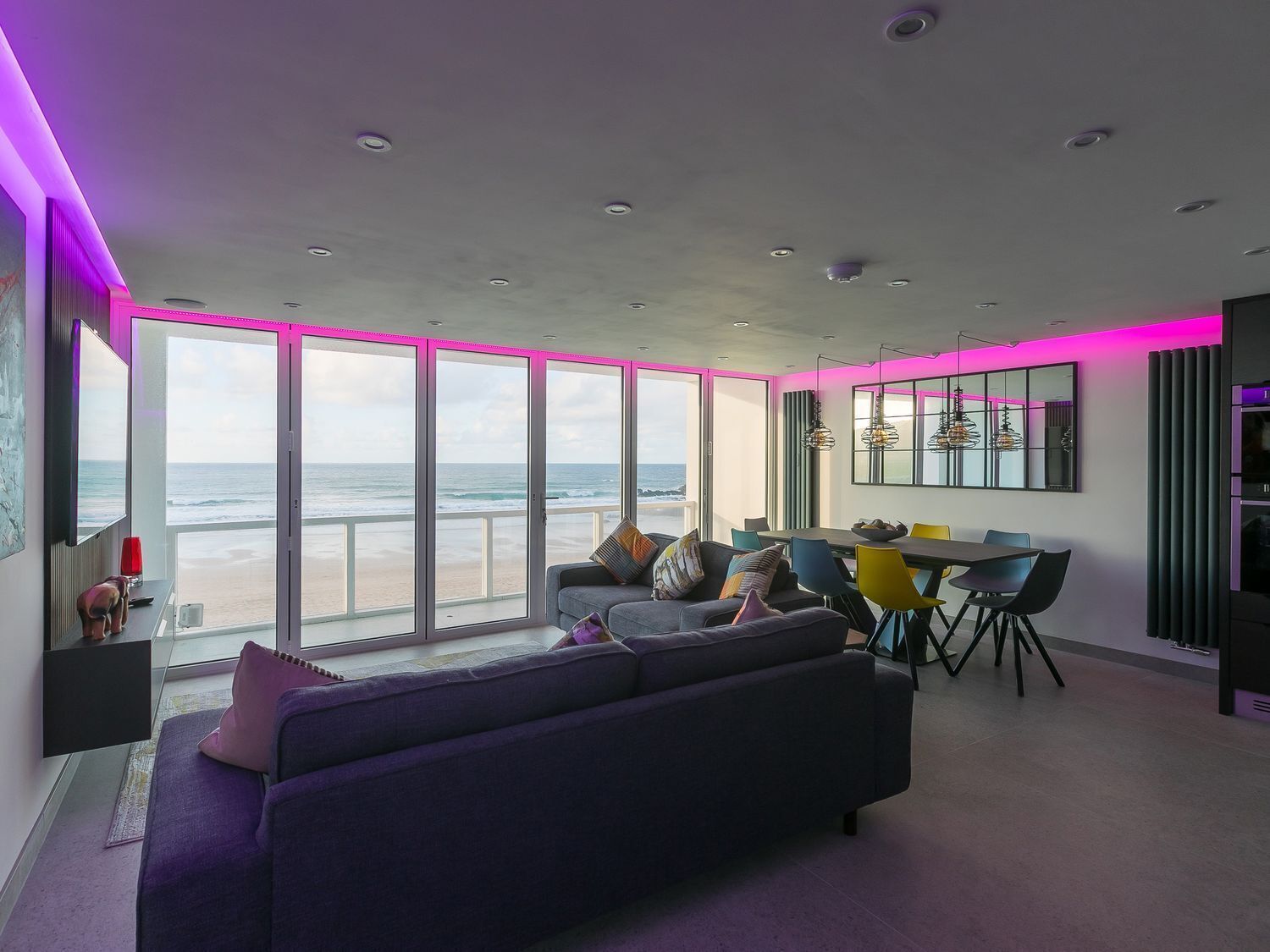 Ett modernt vardagsrum med en stor soffa, en matplats och utsikt över stranden.