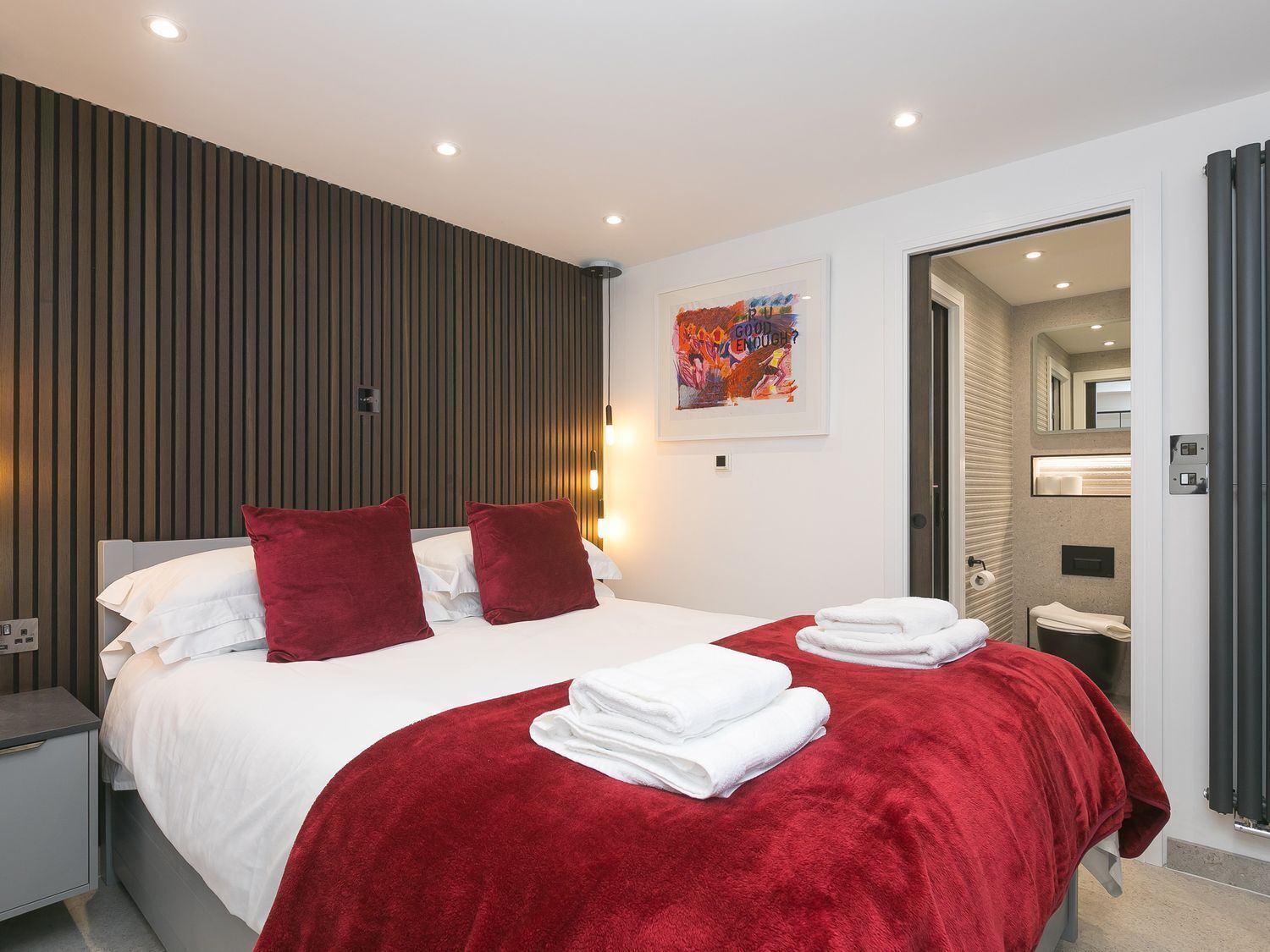 Una habitació d'hotel moderna amb un llit gran, roba de llit vermella i blanca, una manta vermella i un quadre a la paret.