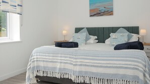 A bedroom with a bed, pillows, a painting, and a window with curtains.
