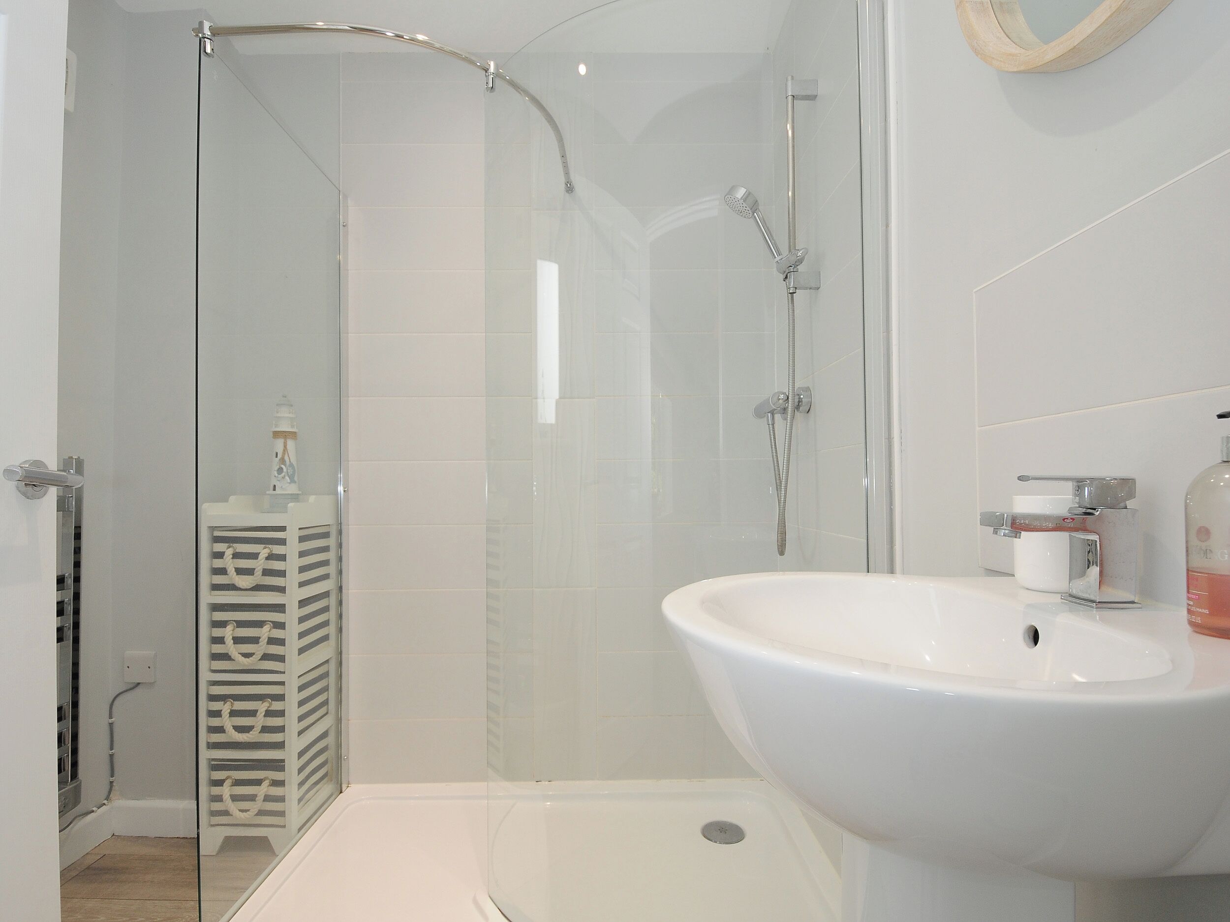 A modern bathroom with a glass shower enclosure, a white sink, and a storage unit with drawers.