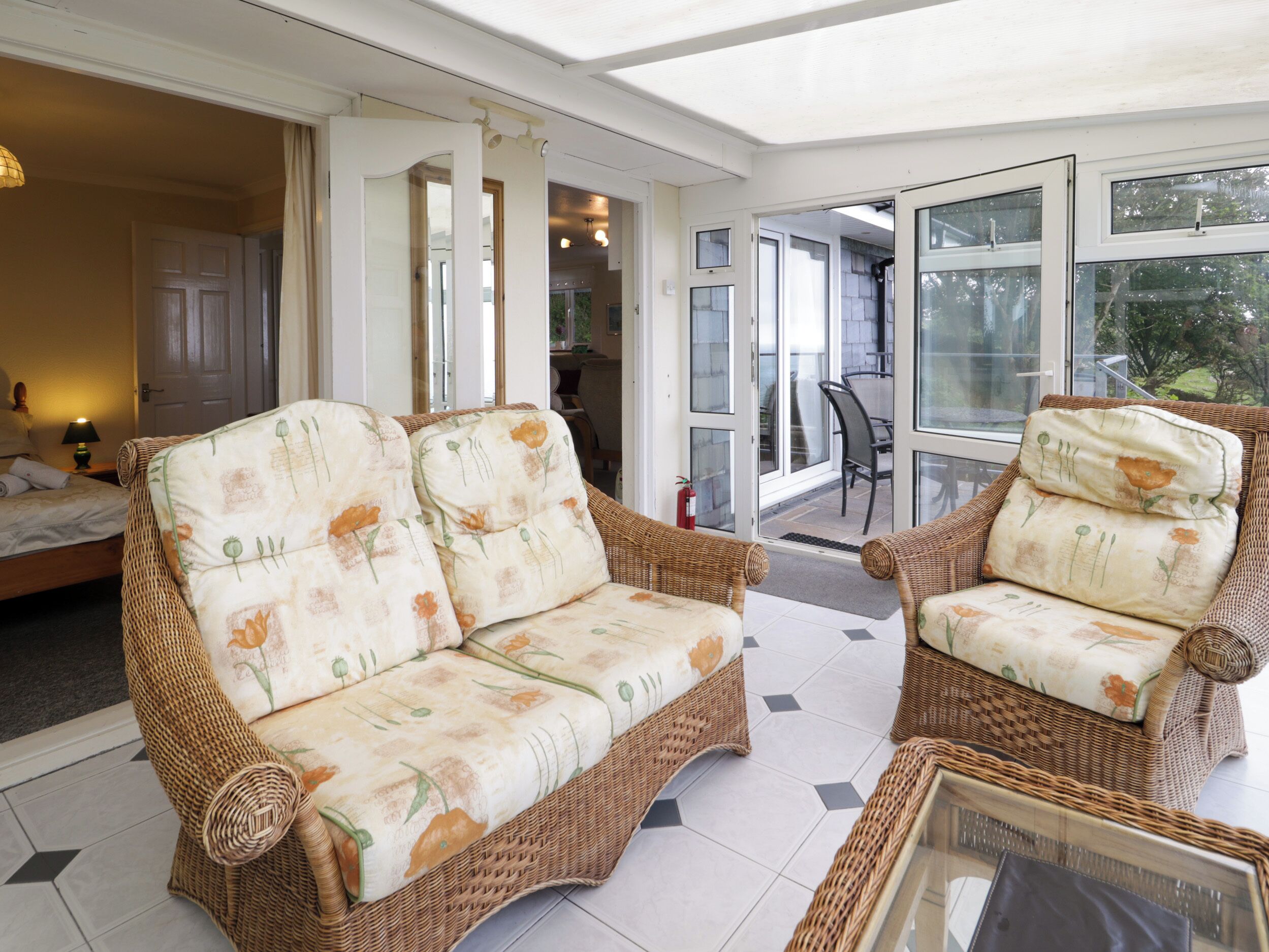 A sunlit room with wicker furniture, including a sofa and armchairs, and a glass door leading to an outdoor area.