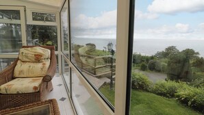 A room with a view of a coastal landscape, including a grassy area and a pathway leading to a sea view. - Woodland Roost (Barmouth)