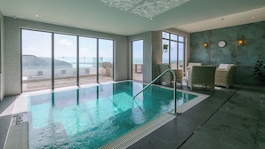 Una piscina interior con vistas despejadas al océano, amplias ventanas y un techo con un diseño de iluminación singular.