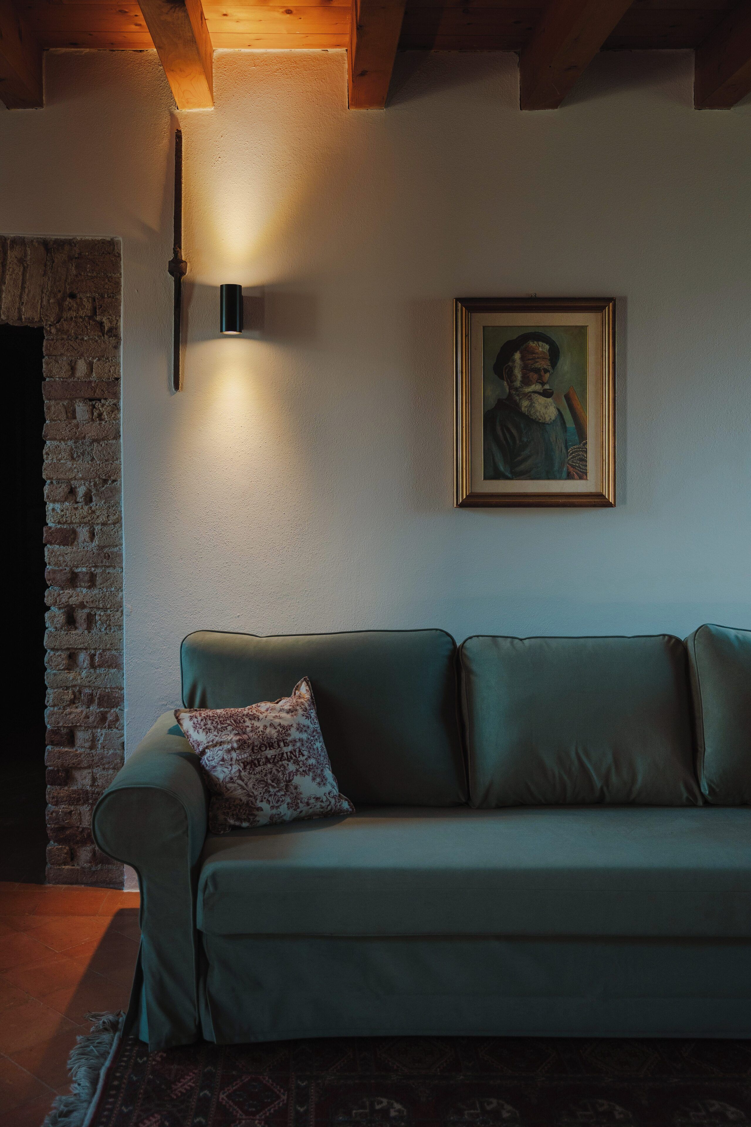 Un salon chaleureux avec un canapé vert, un coussin à motifs, un tableau encadré et un luminaire fixé au mur.
