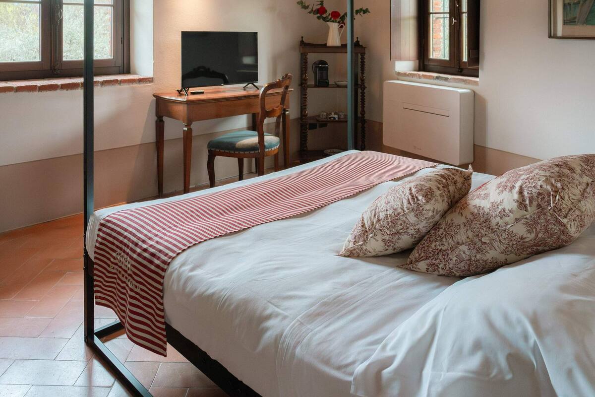 Una camera da letto con un letto a baldacchino, una scrivania con una sedia, una televisione e una finestra che offre vista sull'esterno.