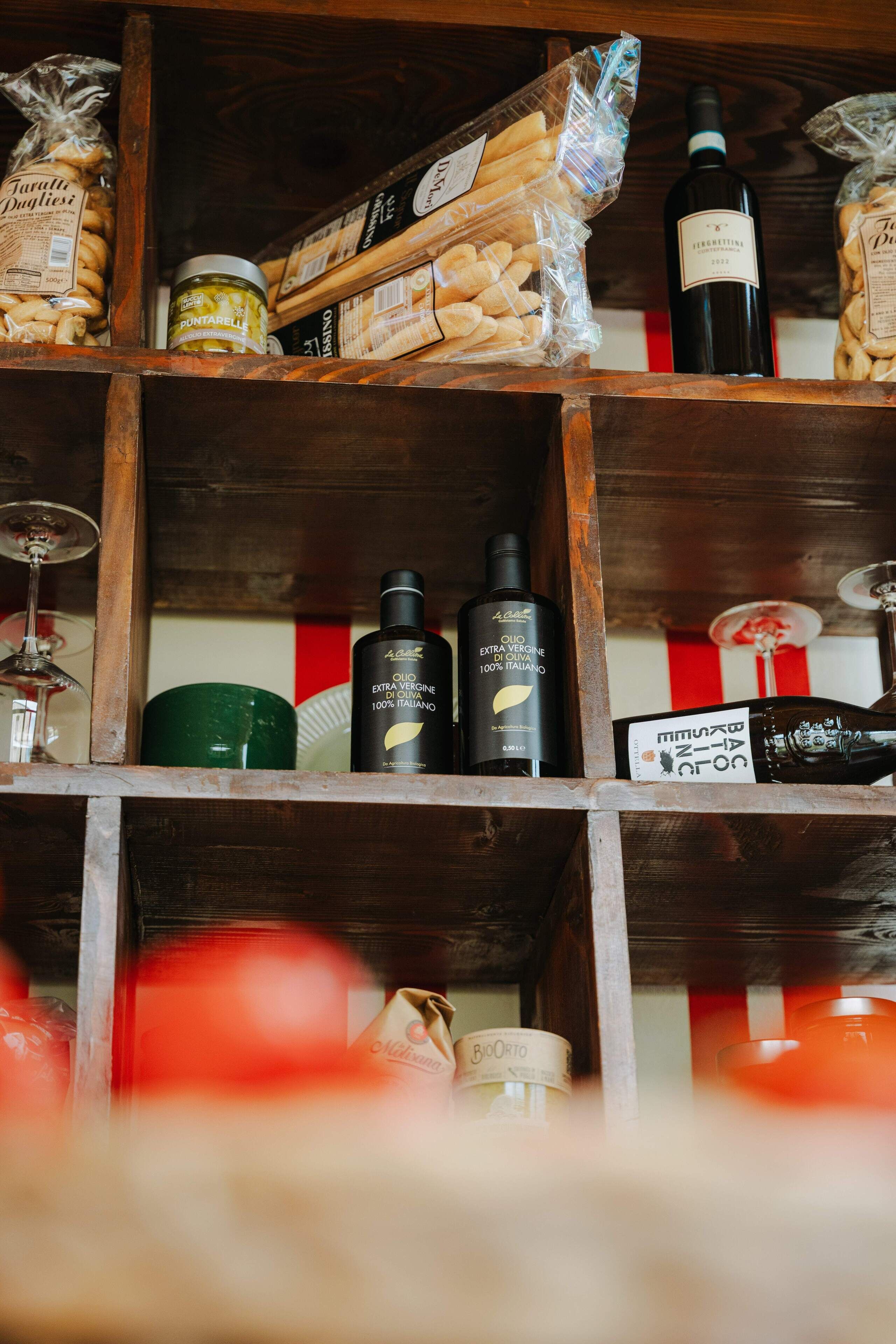 A wooden shelf with various food items and bottles, including pasta, olive oil, and wine.