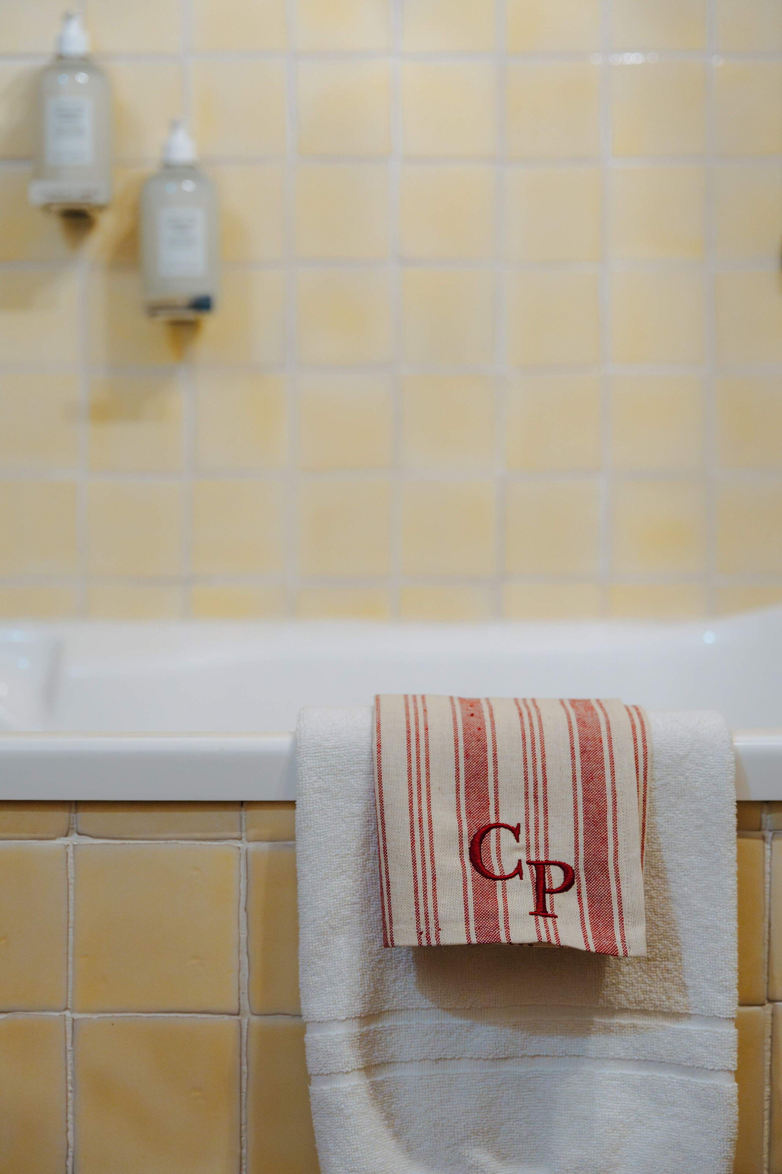Une salle de bain avec des carreaux jaunes, une baignoire blanche et une serviette à rayures rouges et blanches, posée sur un porte-serviettes.