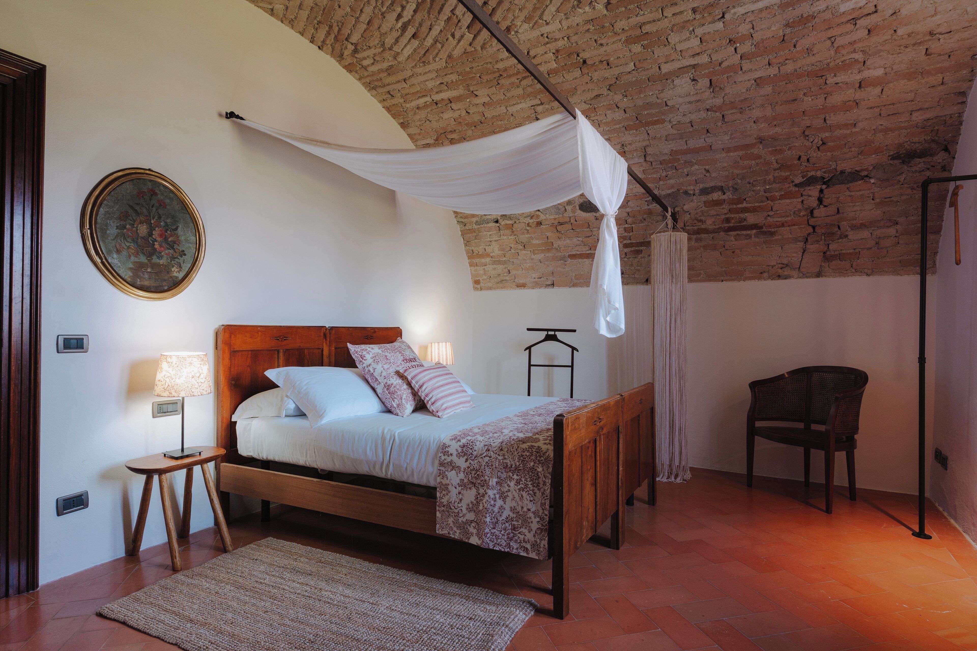 Un dormitorio con una cama de madera, una mesita de noche, una lámpara, una silla y un techo de ladrillo.