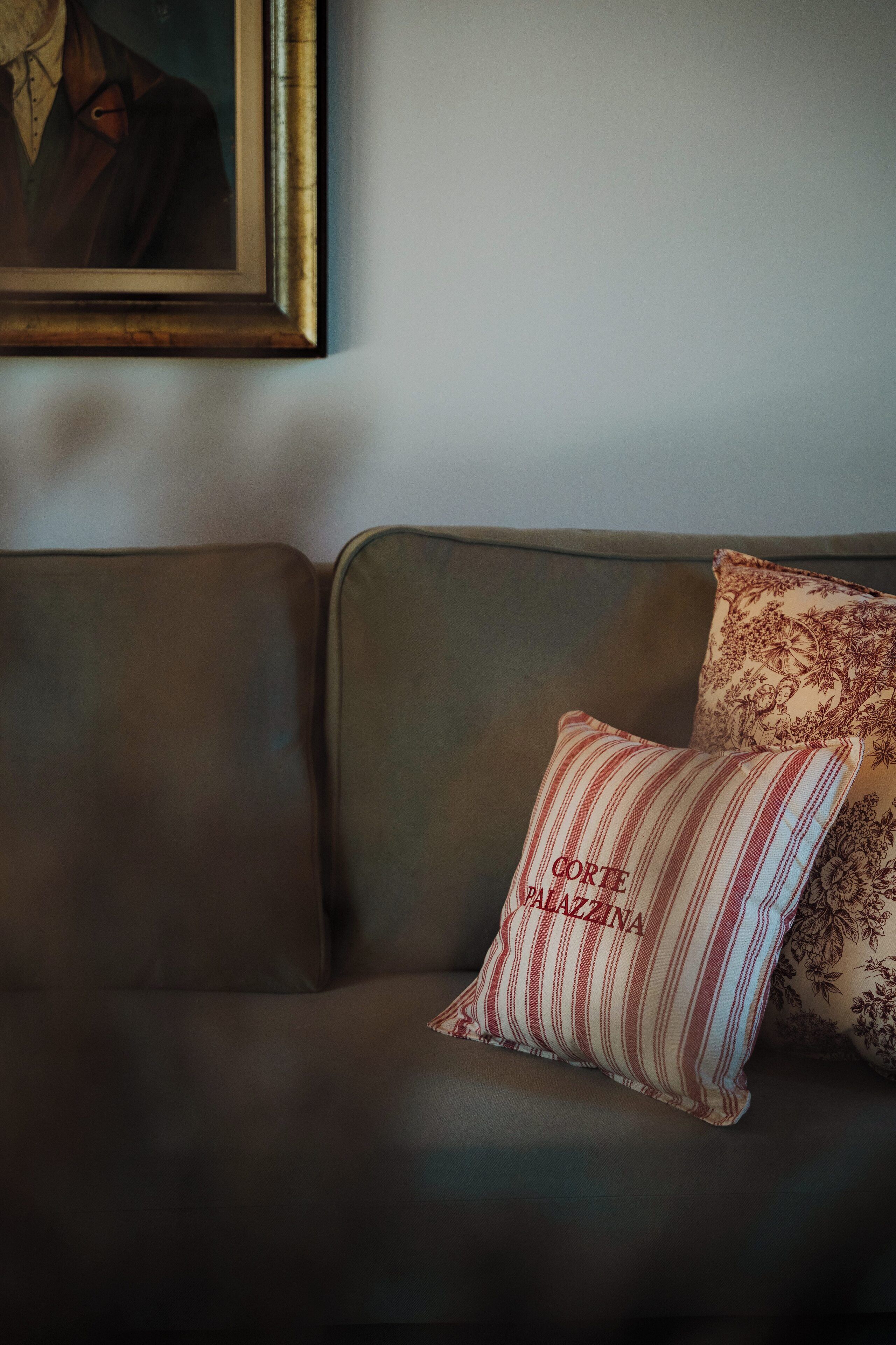 A dark brown sofa with two pillows, one striped and one with a floral pattern, and a framed portrait above it.