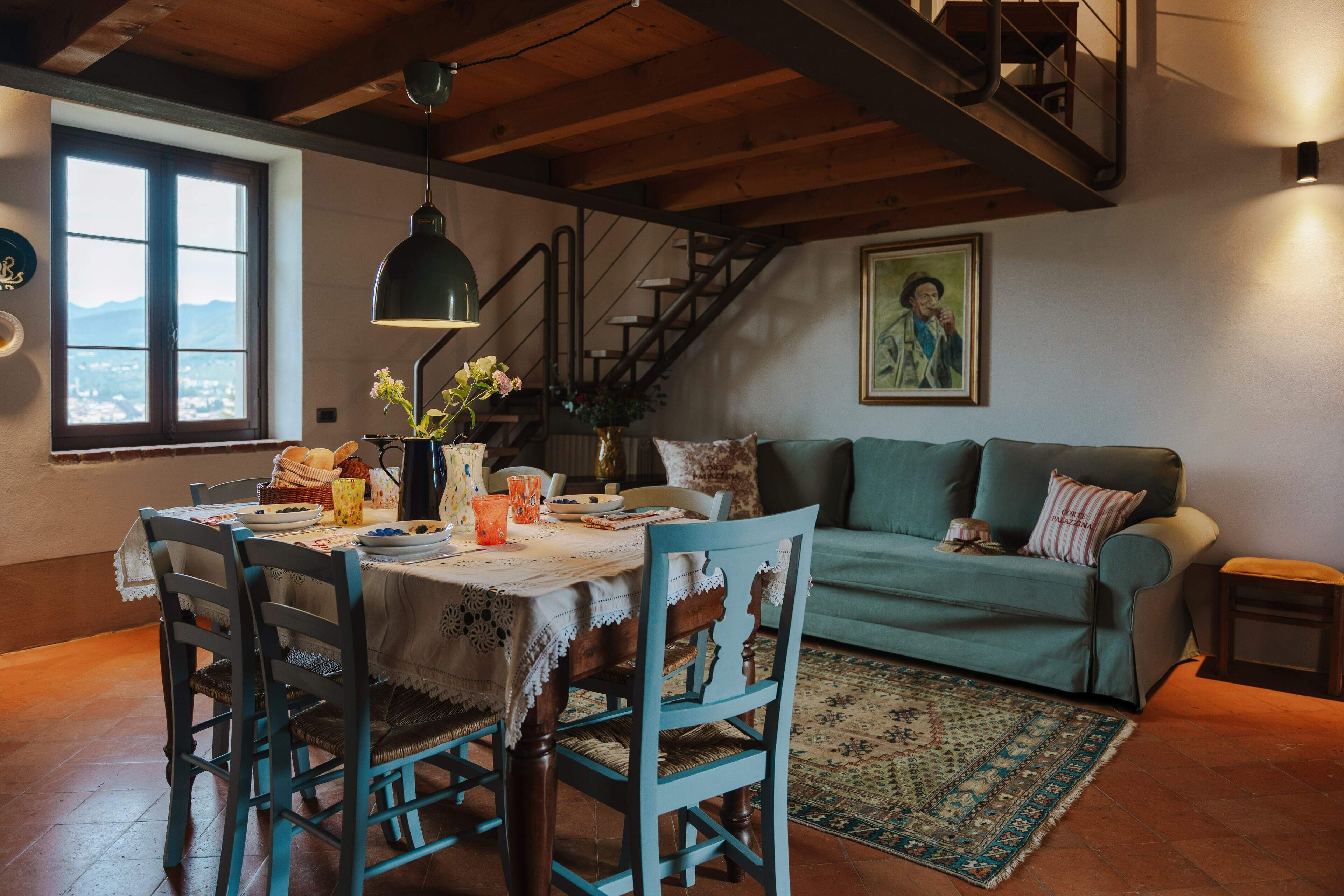 Un coin repas avec une table dressée pour quatre personnes, un canapé vert et un escalier menant à un niveau supérieur.