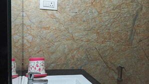 Une salle de bain avec un mur en marbre, un lavabo blanc, un miroir et une douche.