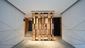 Een moderne hal met een geometrisch wandontwerp, een houten scheidingswand en een trap naar een andere ruimte.