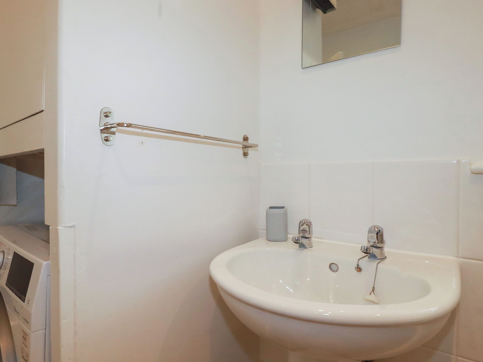 Een badkamer met een wit wastafelmeubel, een spiegel erboven en een handdoekrek.