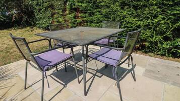 A metal table with four chairs, each with a cushion, set on a stone patio.