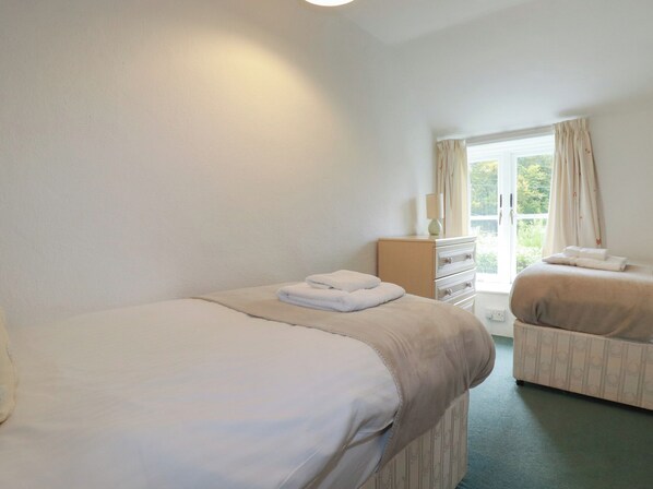 A hotel room with two beds, a dresser, and a window with curtains. - Honeysuckle Cottage (St Austell)