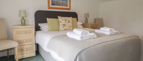 A neatly made bed with a quilted cover, two bedside tables with lamps, a chair, and a framed picture on the wall.