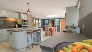 A modern kitchen with a central island, bar stools, and a dining area with a table and chairs. - Thompson Rigg House (Scarborough)