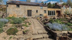 A stone house with a tiled roof, a wooden gate, and a garden with various plants and flowers. - Thompson Rigg House (Scarborough)