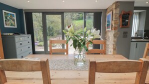 A dining area with a wooden table and chairs, a vase with flowers, and a view of greenery through large windows. - Thompson Rigg House (Scarborough)