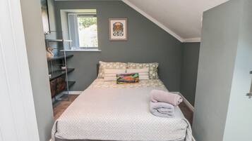 Una camera da letto con un letto, una finestra, un quadro appeso e una mensola con diversi oggetti.