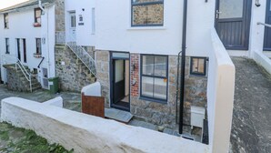 Un edificio blanco de fachada de piedra, con una escalera de madera y una puerta con ventanal.