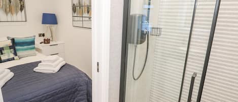 Une chambre à coucher moderne, avec un lit, une table de chevet, une lampe et une étagère murale agrémentée d’objets décoratifs.