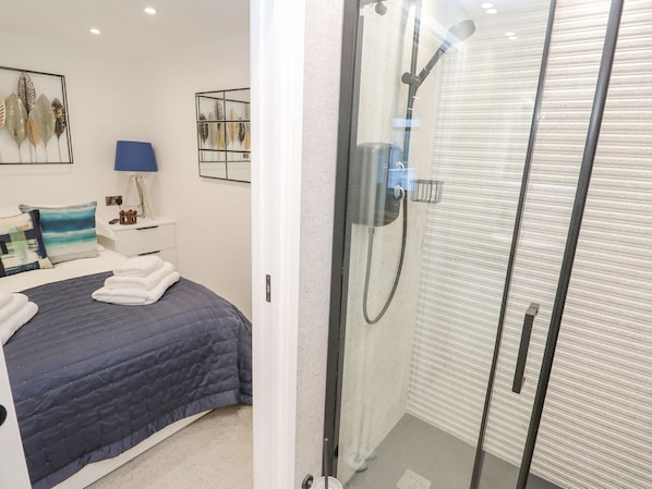 A modern bedroom with a bed, a bedside table, a lamp, and a wall-mounted shelf with decorative items.