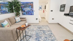 Un salón moderno con un sofá, una mesita de centro con croissants, una alfombra azul y blanca y un cuadro en la pared.