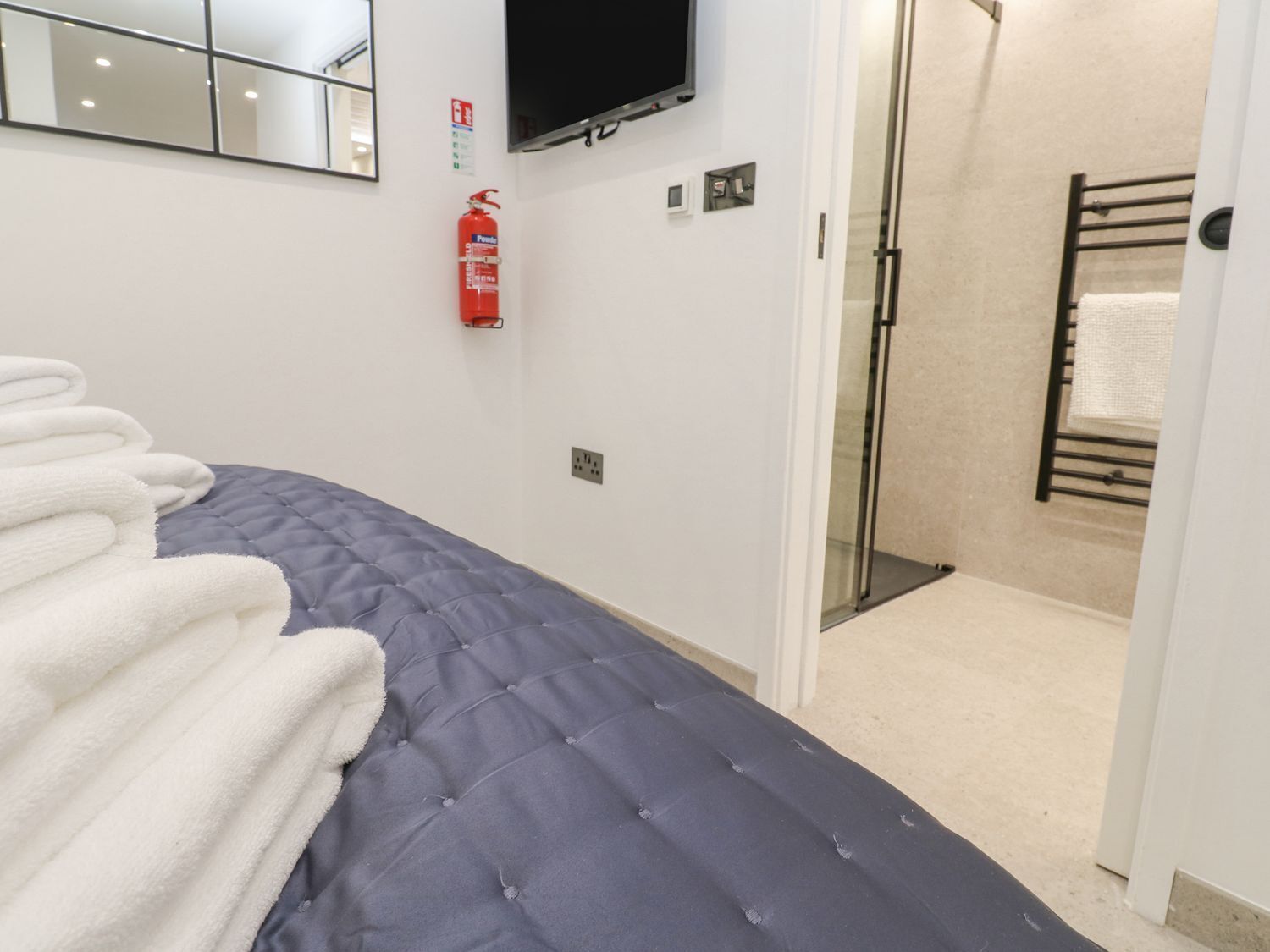 A hotel room with a bed, a fire extinguisher, a television, and a shower area.