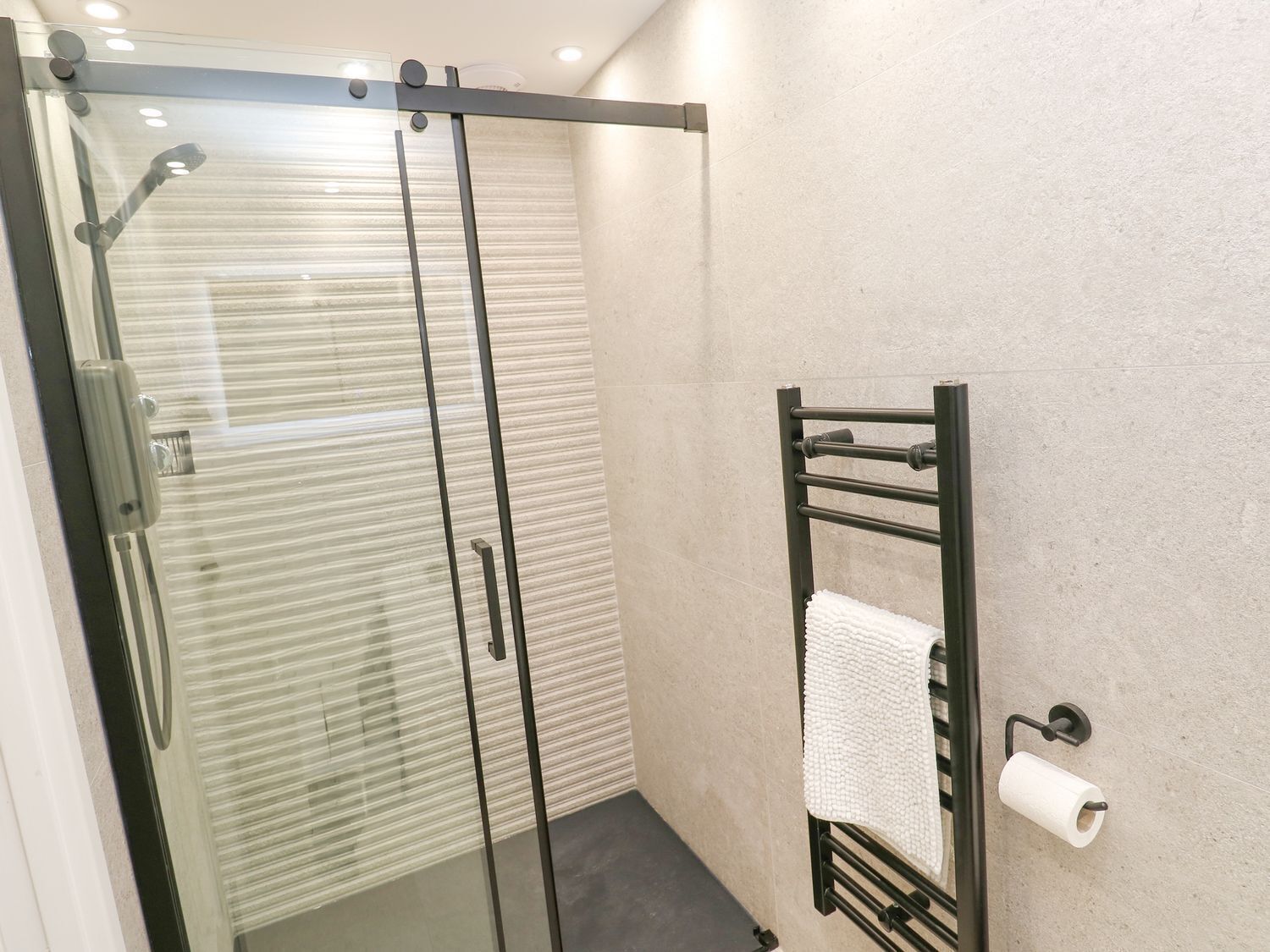 Une douche fermée par des parois en verre, avec un porte-serviettes et un support à papier toilette.