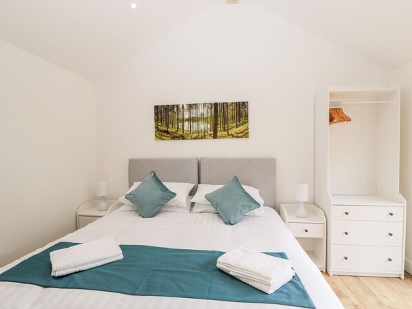A modern bedroom with a large bed, two nightstands, a white dresser, and a forest-themed wall art.