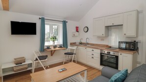 Un espacio habitable compacto con kitchenette, un comedor con mesa y sillas, un sofá y un televisor montado en la pared.