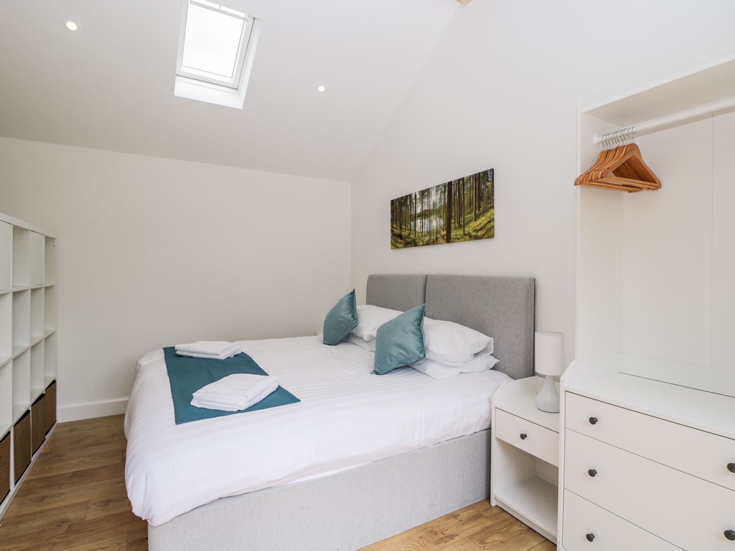 A bedroom with a bed, a nightstand, a dresser, a window, and a wall-mounted picture.