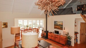 A spacious living room with a large window, a fireplace, a dining area, and a modern chandelier. - Roughtor Barn (Camelford)