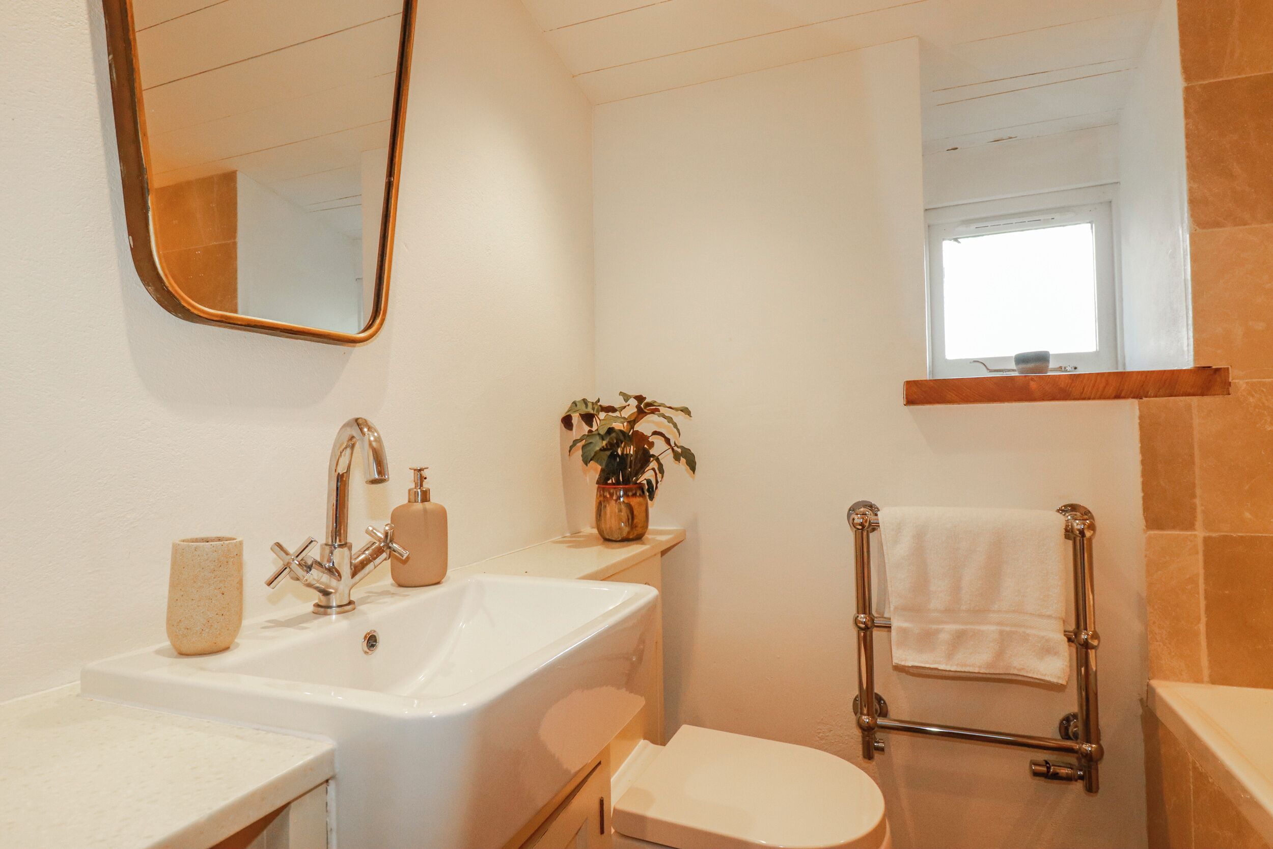 A bathroom with a sink, mirror, toilet, towel rack, and a window.