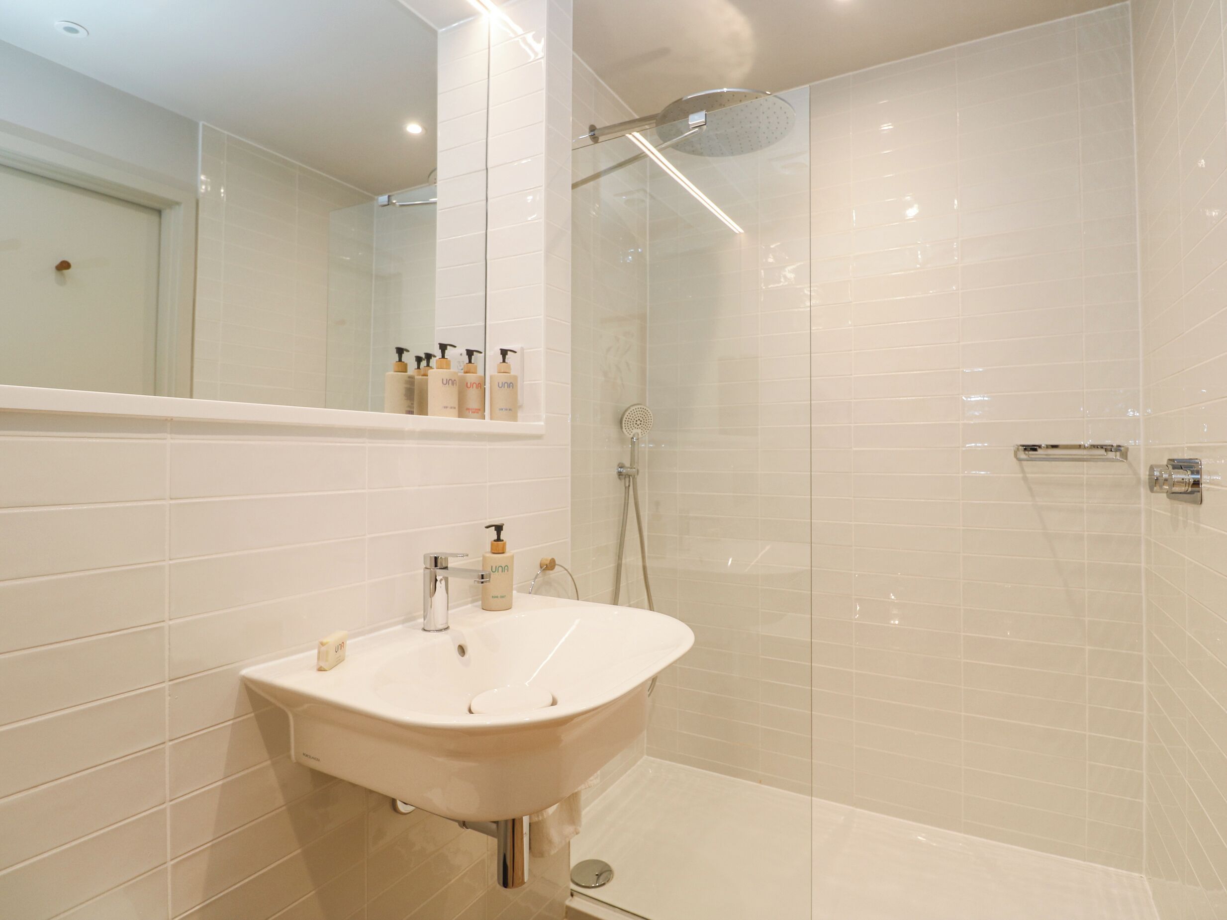 A modern bathroom with a white sink, mirror, and shower.