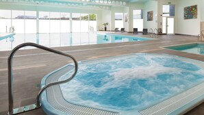 Piscina interna com hidromassagem, teto transparente com aberturas circulares e vista para o exterior.