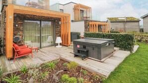 Uma casa moderna com deck de madeira, banheira de hidromassagem e área de estar externa com móveis.