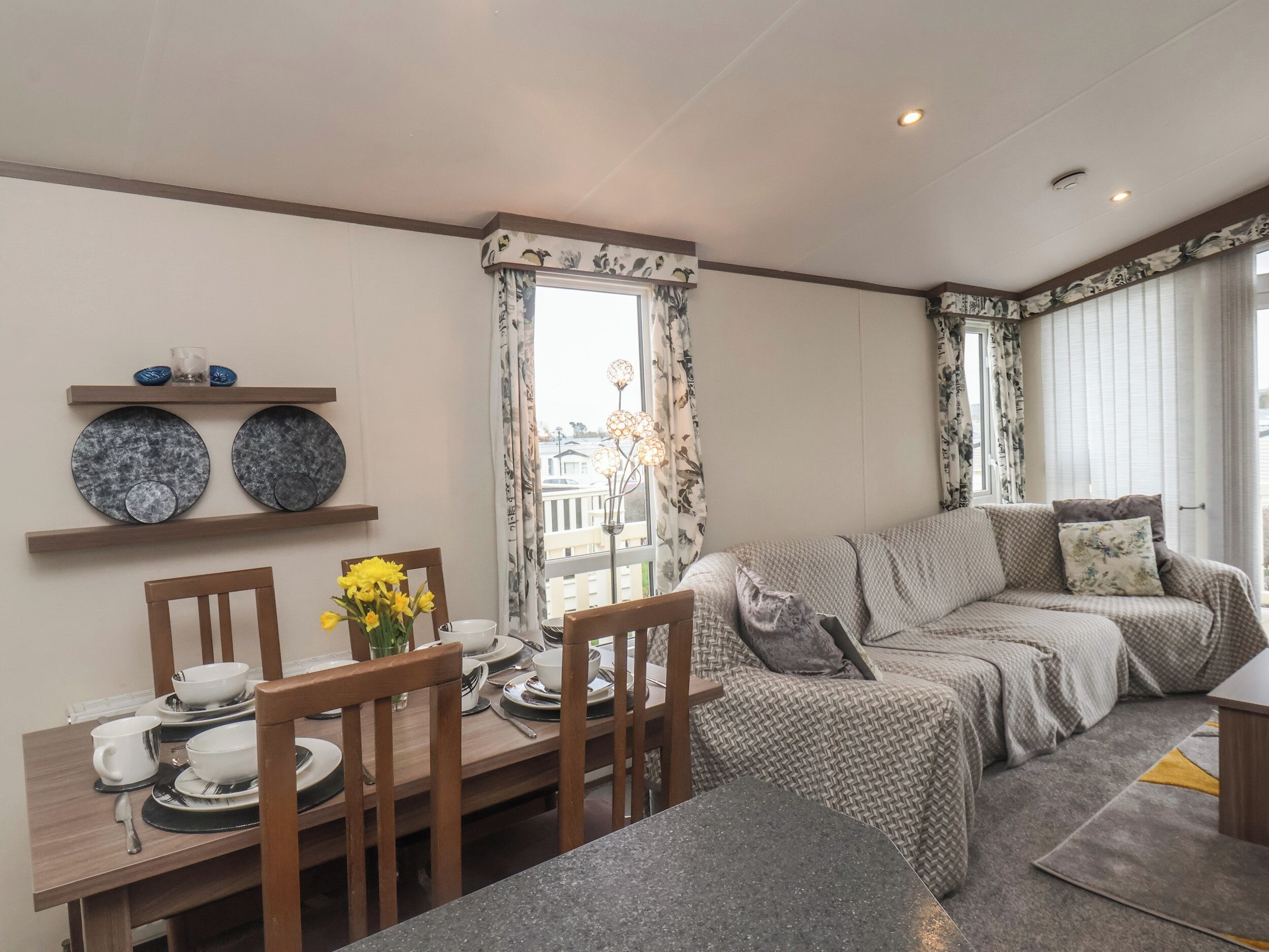 Ein modernes Wohnzimmer mit einer Couch, einem Esstisch und Stühlen. Es gibt ein Fenster mit Vorhängen, eine dekorative Leuchte und einen Blick nach draußen.
