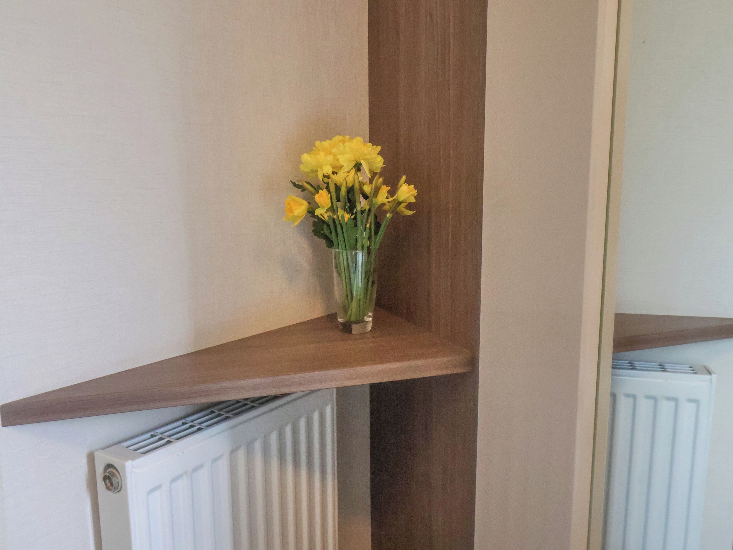 A corner shelf with a vase of yellow flowers.