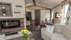A modern living room with a sofa, a coffee table, a fireplace, and a kitchen area visible through an open door. - 47 The Drake Forgetmeknot (Scarborough)