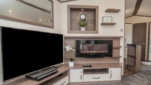 A modern living room with a large flat-screen TV, a fireplace, a clock, and a small plant on a shelf. - 47 The Drake Forgetmeknot (Scarborough)