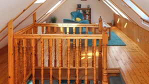 A wooden staircase leading to an attic bedroom with a blue chair and a bookshelf. - Jade Cottage (Macduff)