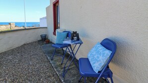 A small outdoor seating area with two blue chairs and a table, a potted plant, and a view of the sea. - Jade Cottage (Macduff)