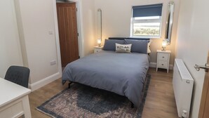 Un dormitorio con cama, mesitas de noche, escritorio, silla, ventana y radiador.