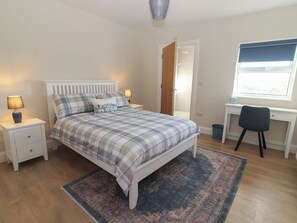 Un dormitorio con cama, mesitas de noche, escritorio y silla.