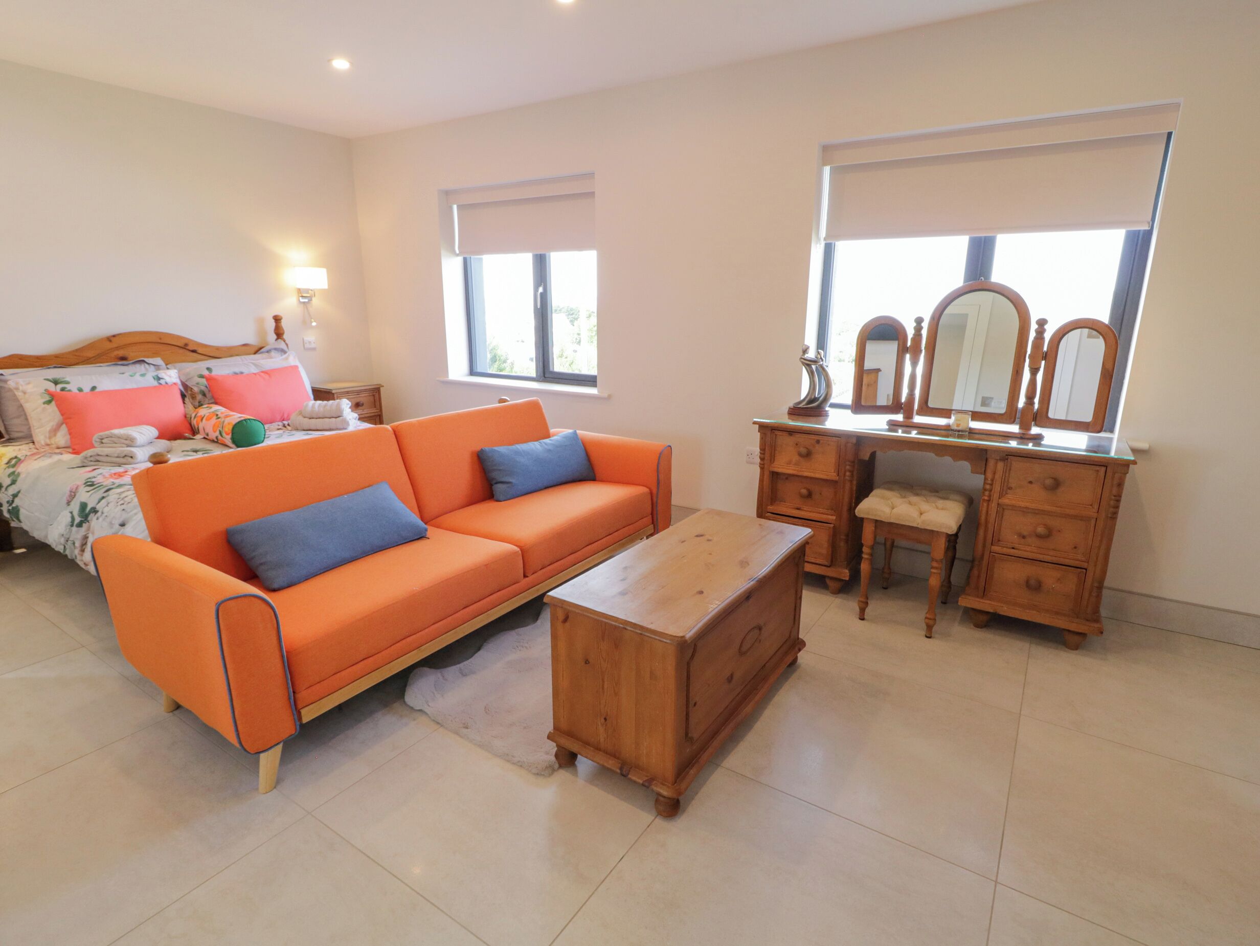 Een slaapkamer met een bed, een oranje bank, een houten dressoir en een nachtkastje.