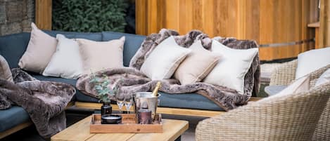 Un espace de détente extérieur accueillant, avec un canapé, des coussins, une table basse en bois et un jacuzzi en arrière-plan.