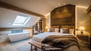 Una camera da letto con una finestra sul tetto, un letto grande, una vasca da bagno e rivestimenti in legno.