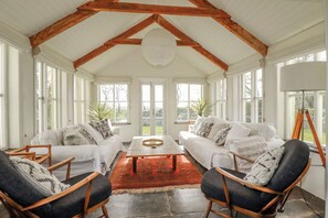 A sunroom with white furniture, a red rug, and wooden beams. - Poldue House (Camelford)